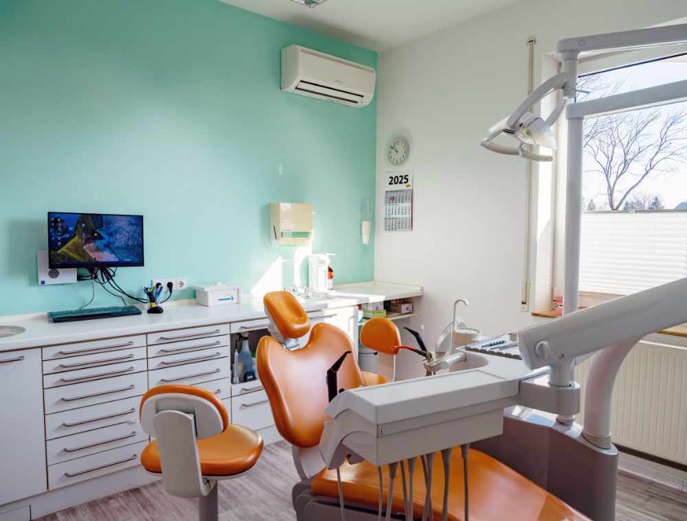 Modernes Behandlungszimmer mit orangefarbenem Behandlungsstuhl, Monitor und türkisfarbener Wand.